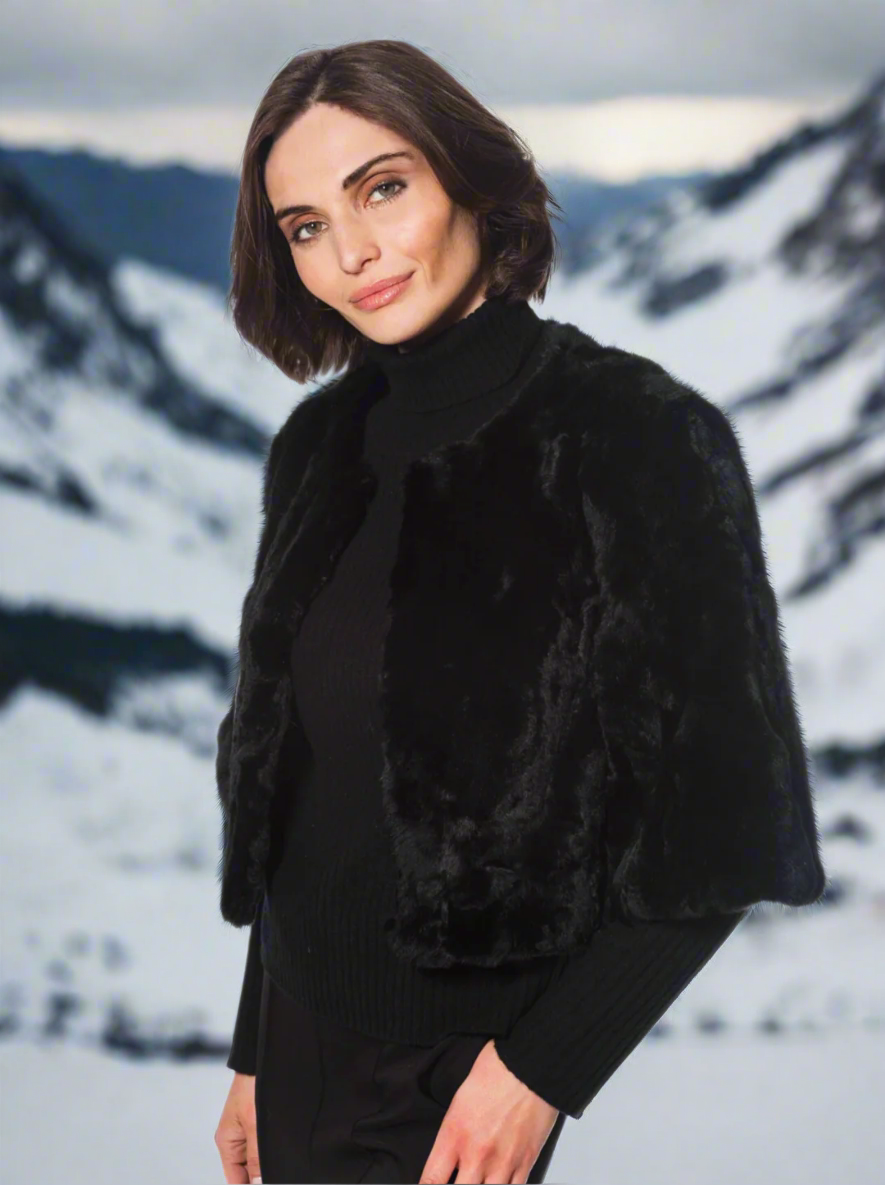 Woman wearing a black fur shrug over a black outfit on a white background