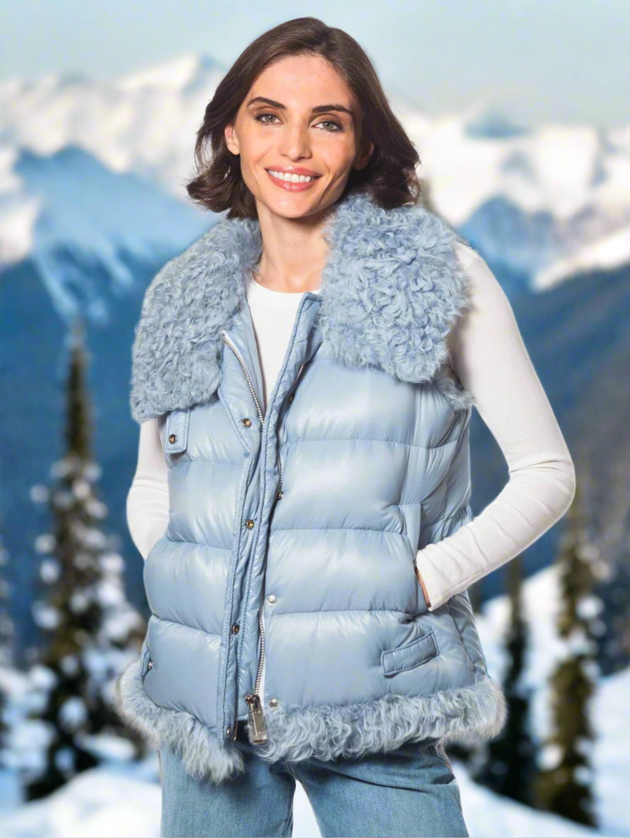 Woman wearing a light blue puffer vest with fur trim in a snowy mountain landscape