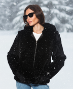 A woman wearing a black Rex Rabbit Fur coat with hood, sunglasses, and blue jeans.