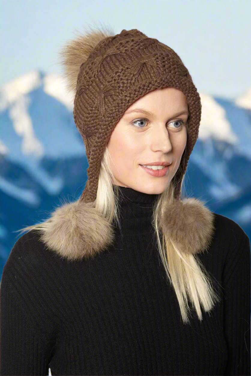 A woman wearing a brown wool hat with three genuine fur poms attached to the brim.