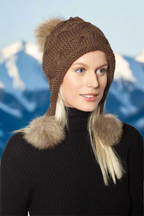 A woman wearing a brown wool hat with three genuine fur poms attached to the brim.